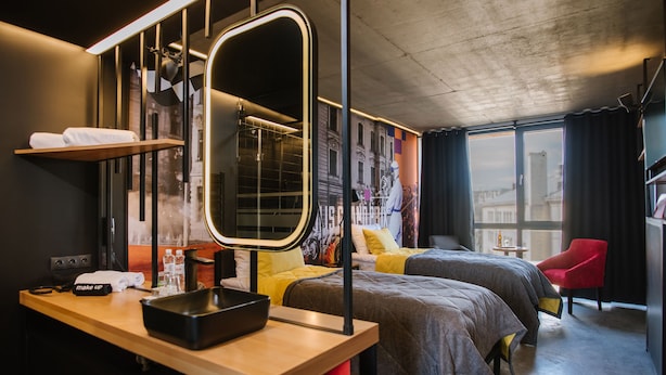 A modern hotel room with two beds, a large mirror, a wooden desk, and a cityscape view. - !FEST Hotel Lemkivska (Lviv)
