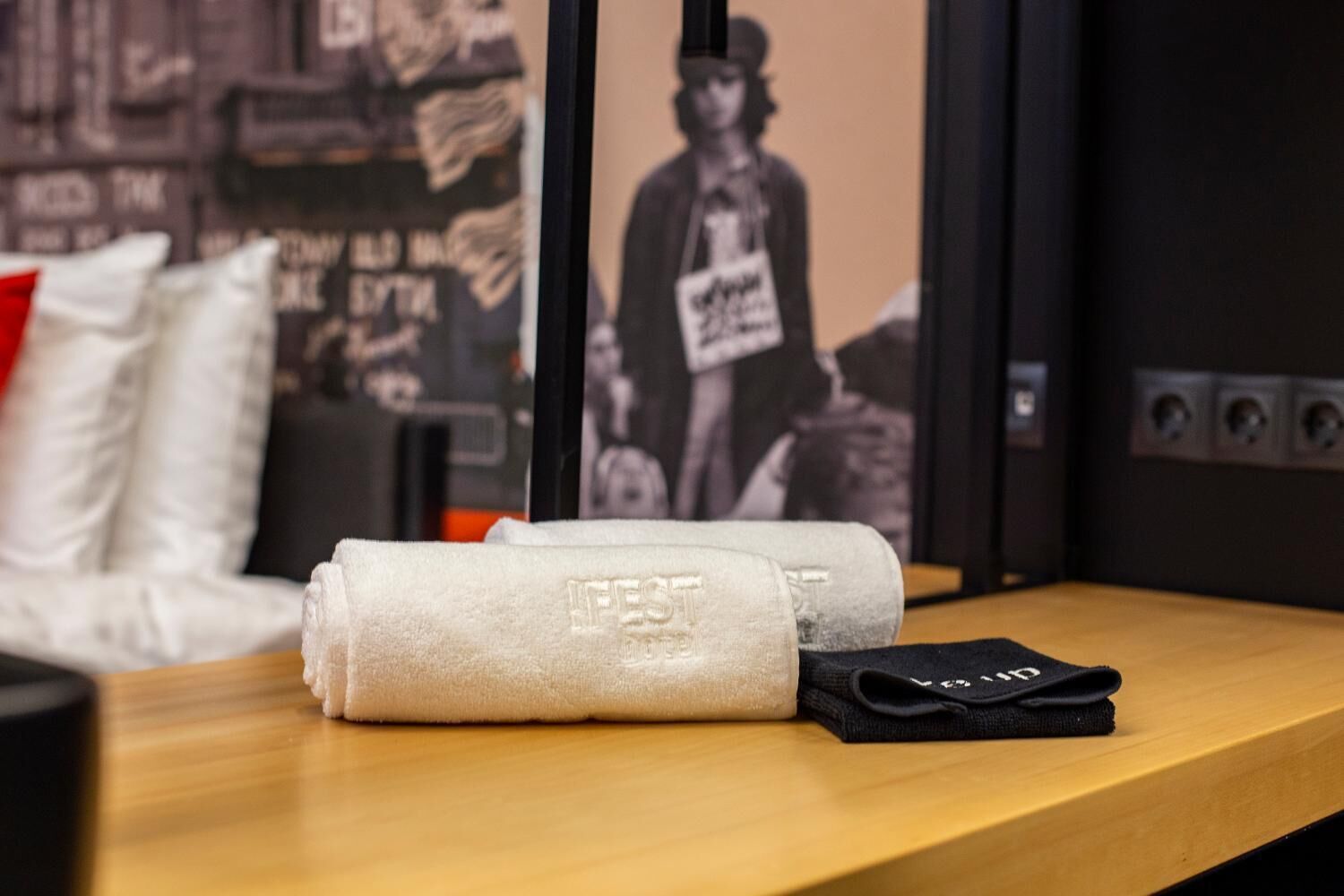 Een netjes gevouwen handdoek met de tekst 'LIFEST' in reliëf, op een houten oppervlak, met een zwart object ernaast.