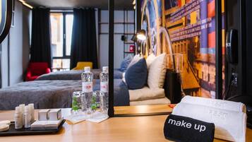 Habitación de hotel con cama, espejo, mesa con artículos de aseo e indicación 'maquillaje'.