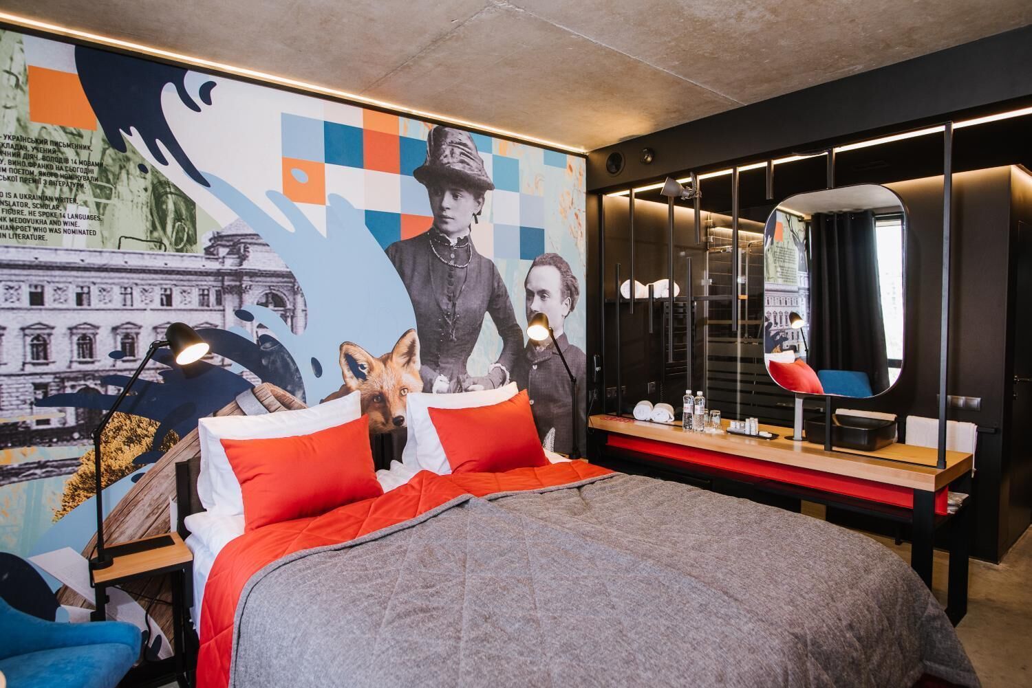 Ein modernes Hotelzimmer mit einem großen Bett, einem Schreibtisch mit Spiegel und einem farbenfrohen Wandgemälde.