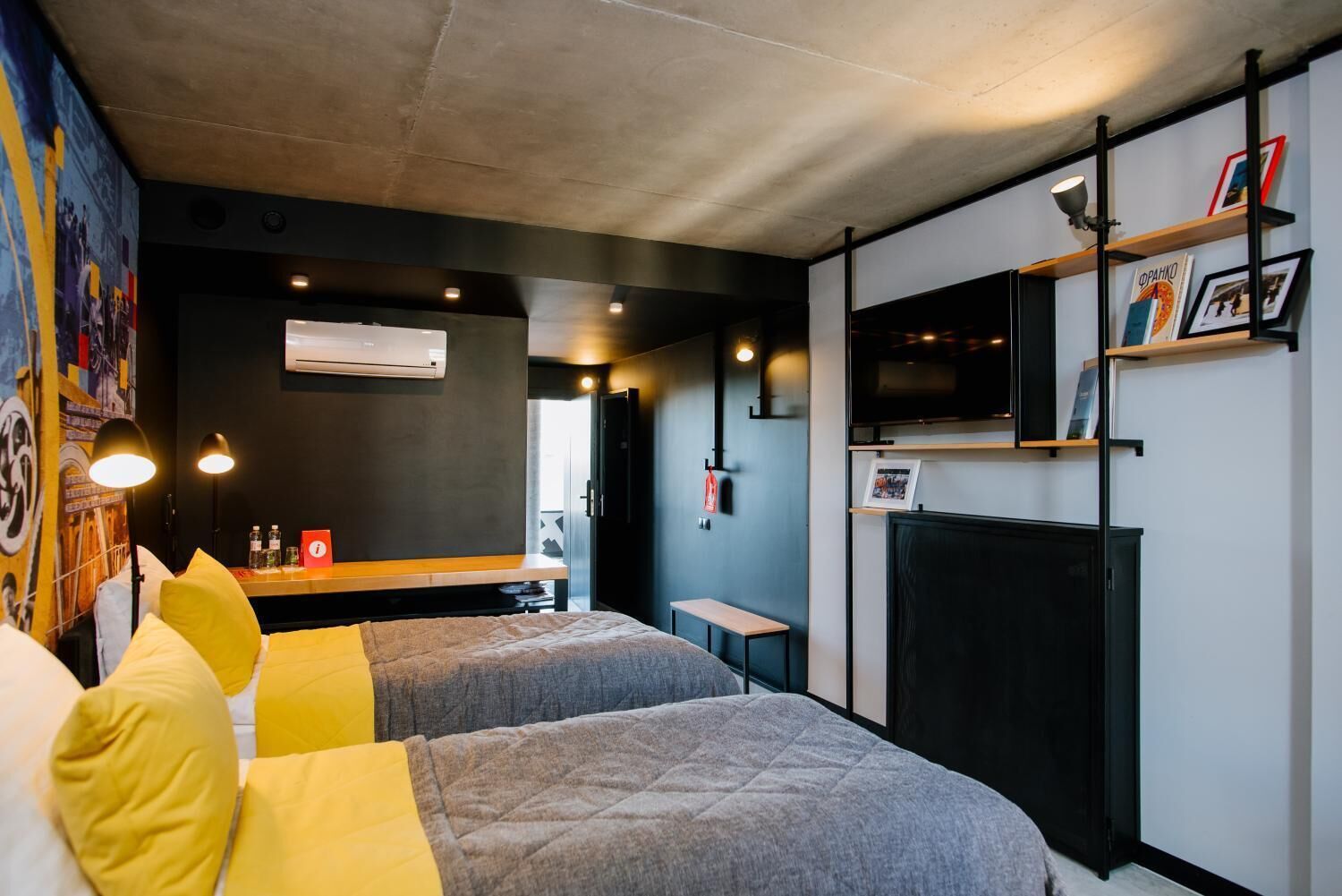 A modern hotel room with two beds, a small table, a TV, and a bookshelf.