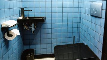 Un baño pequeño con azulejos azules, un lavamanos negro, un dispensador de papel higiénico y un cubo de basura.
