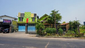 A modern building with a blue gate, a green and yellow facade, and a small garden area. - OYO 1639 Penginapan Anggrek Syariah 1 (Probolinggo)