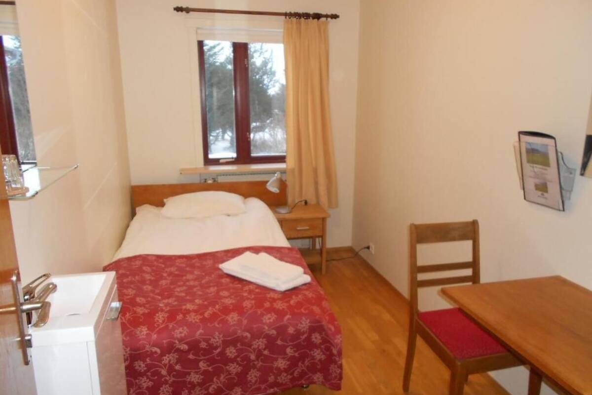 Ein kleines, ordentliches Zimmer mit einem Bett, einem Holztisch, einem Stuhl und einem kleinen Tisch.