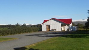 A white barn with a red roof, a gravel path leading to it, and a grassy field in the foreground. - Nes Guesthouse (Borgarbyggd)