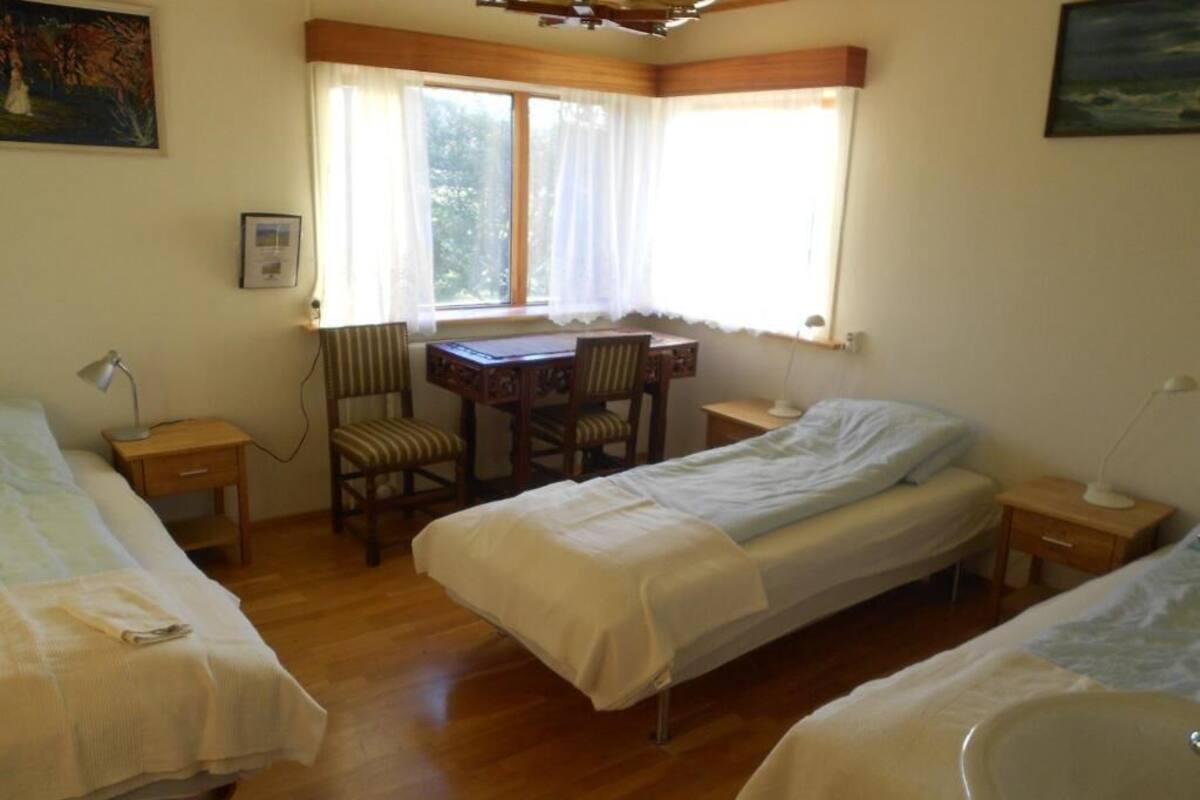 Ein Zimmer mit zwei Einzelbetten, einem Holztisch mit Stühlen, einem Fenster mit Vorhängen und einem Bild an der Wand.