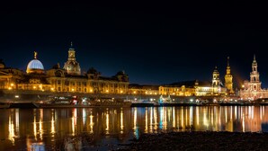 A nighttime cityscape with illuminated buildings reflecting on a calm river. - Ferienwohnung Dresden (Dresden)
