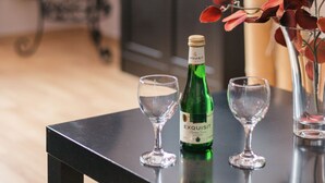 A table with a bottle of Exquisit wine, two empty wine glasses, a decorative vase with red leaves, a birdcage, and a television on a cabinet. - Ferienwohnung Dresden (Dresden)