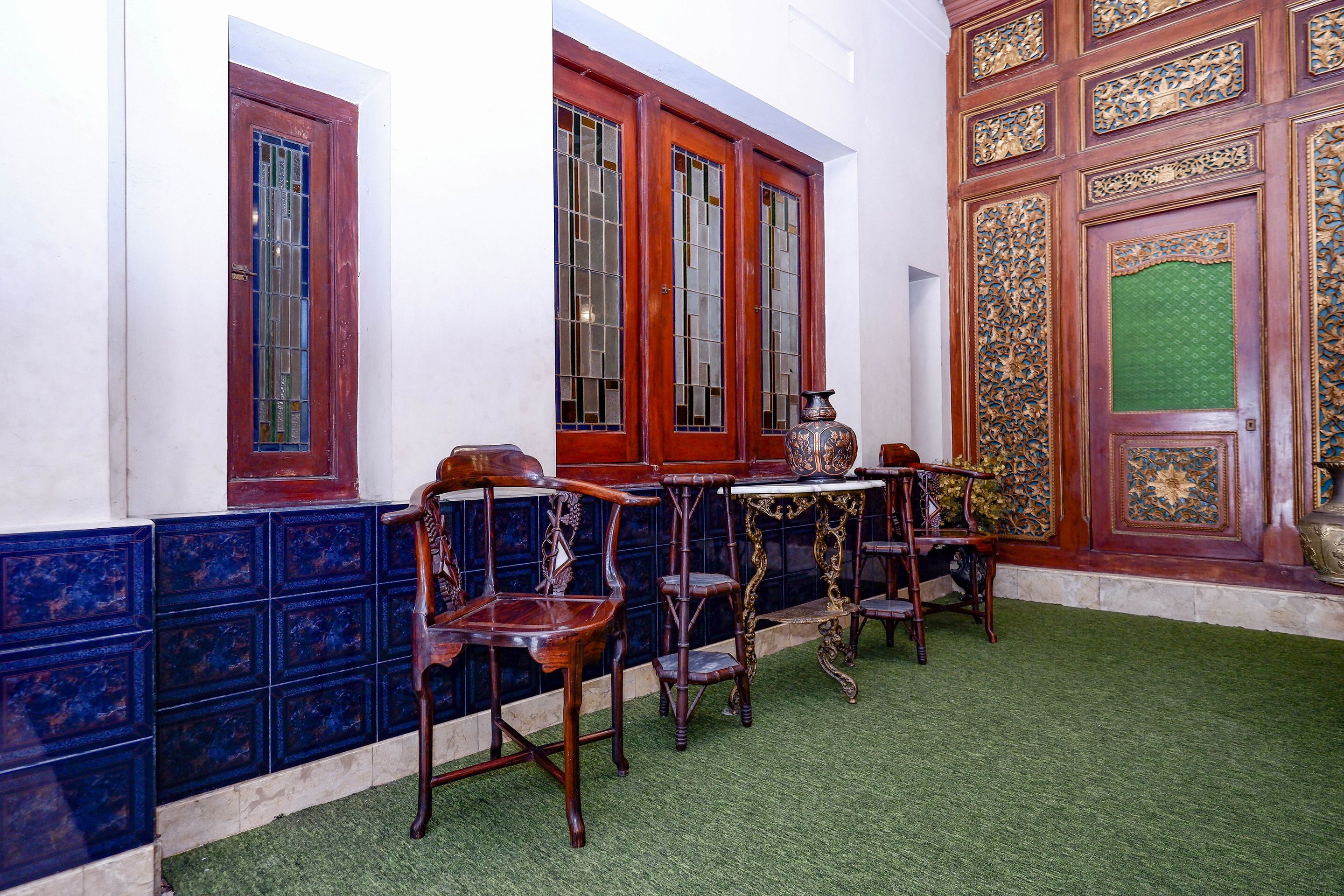 Una habitación con alfombra verde, sillas de madera, una mesa y una puerta decorativa.