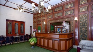 Un espace d’accueil avec un comptoir de réception en bois, un lustre et une moquette verte.