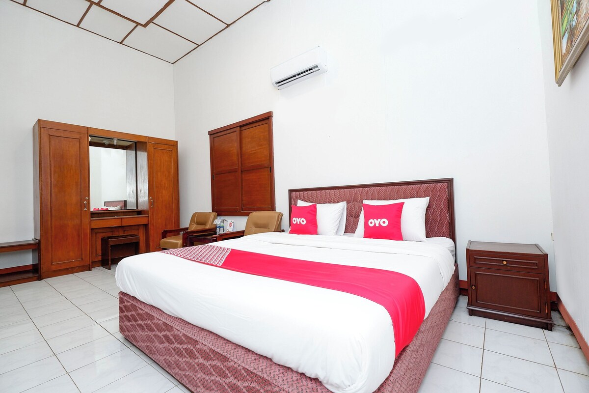 A neatly arranged bedroom with a large bed, a wardrobe, a desk, and a chair.