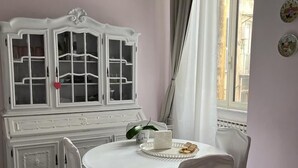 A dining area with a white round table, white chairs, and a white cabinet with glass doors.
