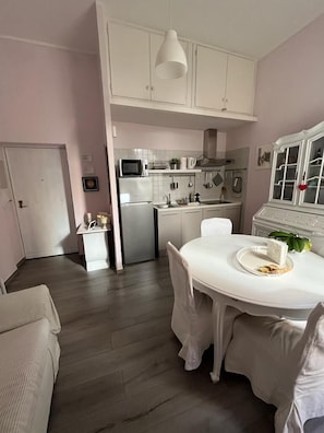 Une cuisine compacte avec des meubles blancs, un four à micro-ondes et un évier. On y trouve une table à manger avec des chaises et une fenêtre donnant sur un beau paysage.