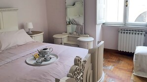 A bedroom with a bed, a bedside table with a lamp, a dresser, a mirror, and a window with a view of the outside.