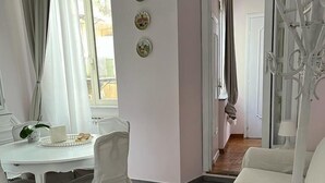 A room with a white dining table, chairs, and a striped sofa. There are three wall-mounted decorations and a door leading to another room.
