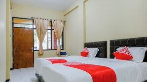 A hotel room with two beds, beige curtains, a wooden door, and a view of the outside. - OYO 1342 Uniga Malang Family Residence (Malang)