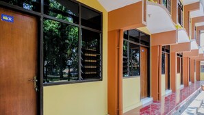 A building with a wooden door, yellow walls, and a red tiled floor. - OYO 1342 Uniga Malang Family Residence (Malang)