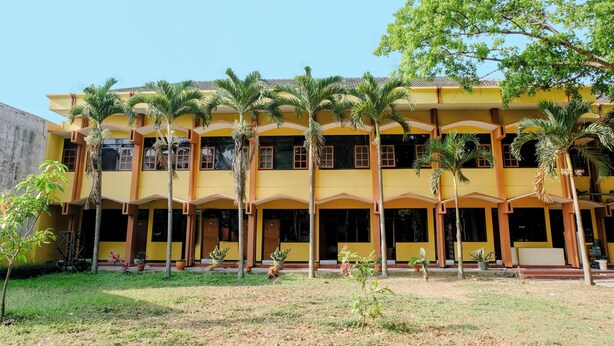 A yellow building with multiple floors, surrounded by palm trees and potted plants. - OYO 1342 Uniga Malang Family Residence (Malang)