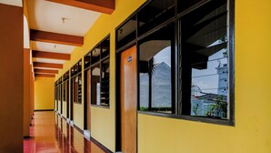 A long corridor with yellow walls and wooden doors, leading to rooms with large windows. - OYO 1342 Uniga Malang Family Residence (Malang)