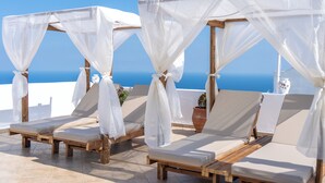 A row of wooden lounge chairs with white canopies, arranged on a terrace with a clear view of the ocean. - Salvatore Caldera Suites (Santorini)