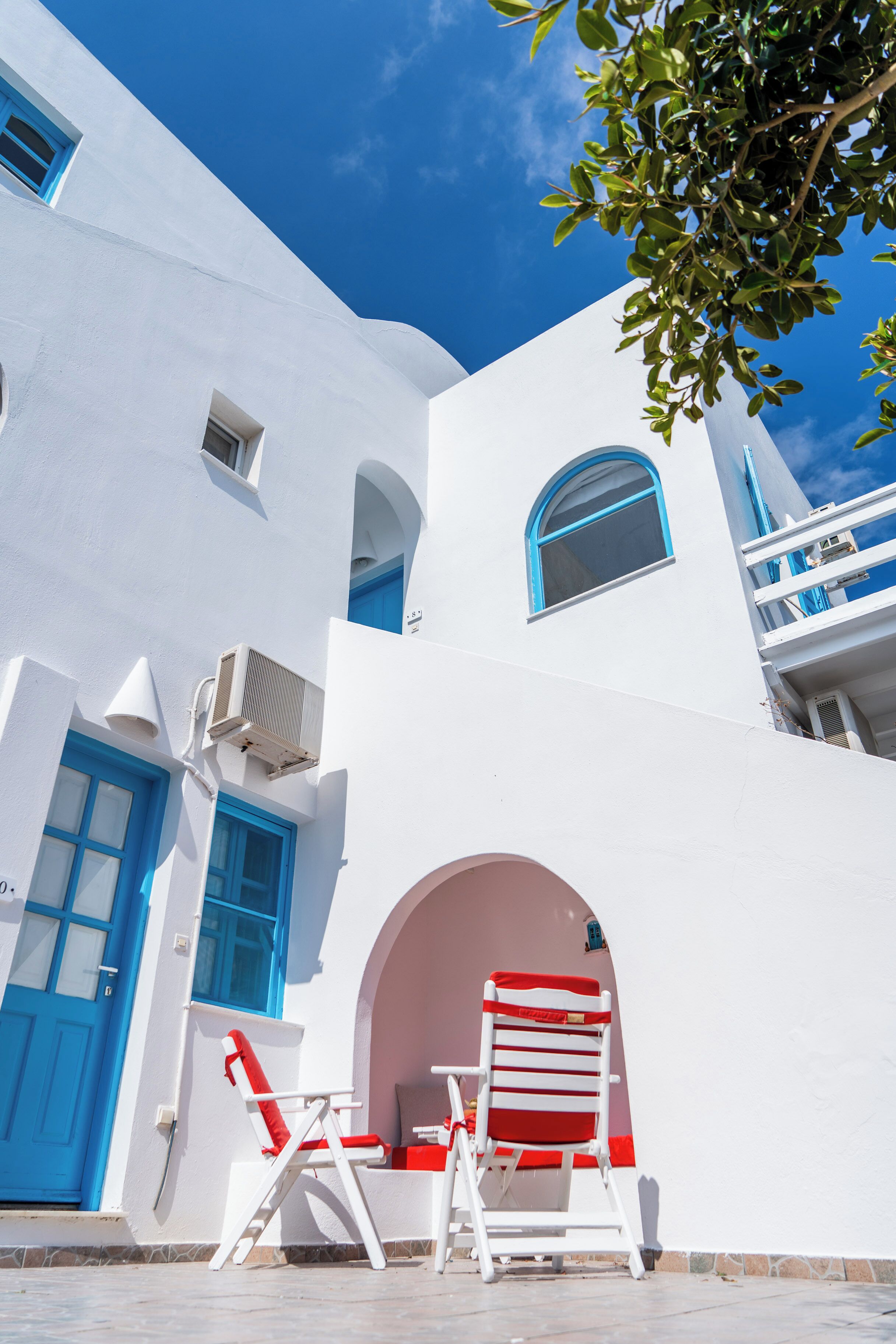 A white building with blue doors and windows, a red and white chair, and an air conditioning unit.