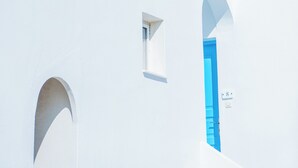 A white building with blue doors and windows, a clear blue sky, and a small flower on the roof. - Salvatore Caldera Suites (Santorini)