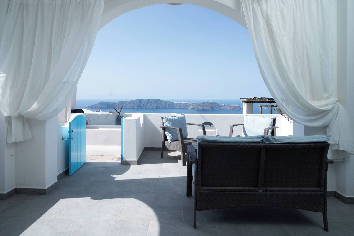 A balcony with white curtains, a wicker sofa, and a view of the sea.