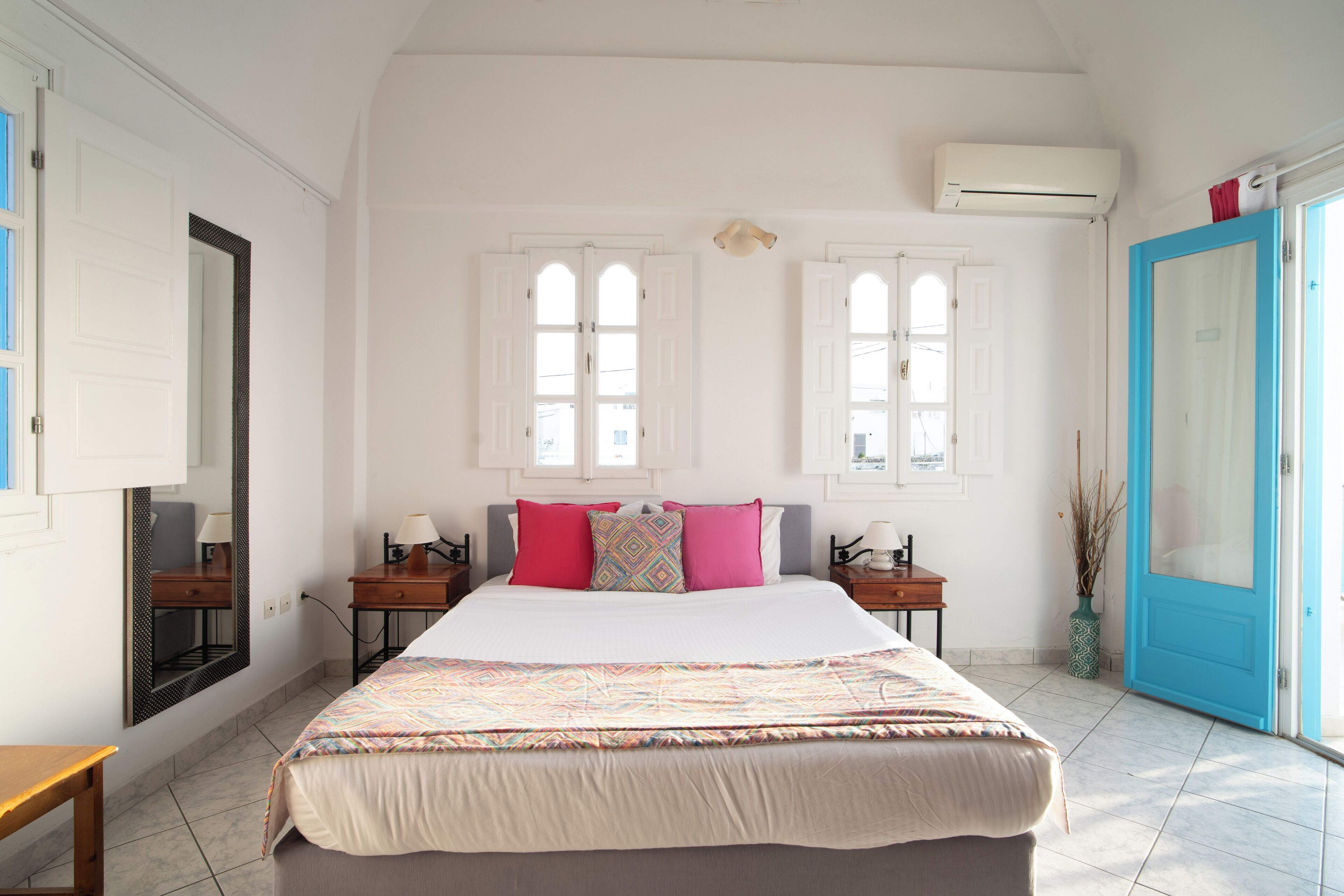 A bedroom with a large bed, two nightstands, a mirror, and a window with a view.