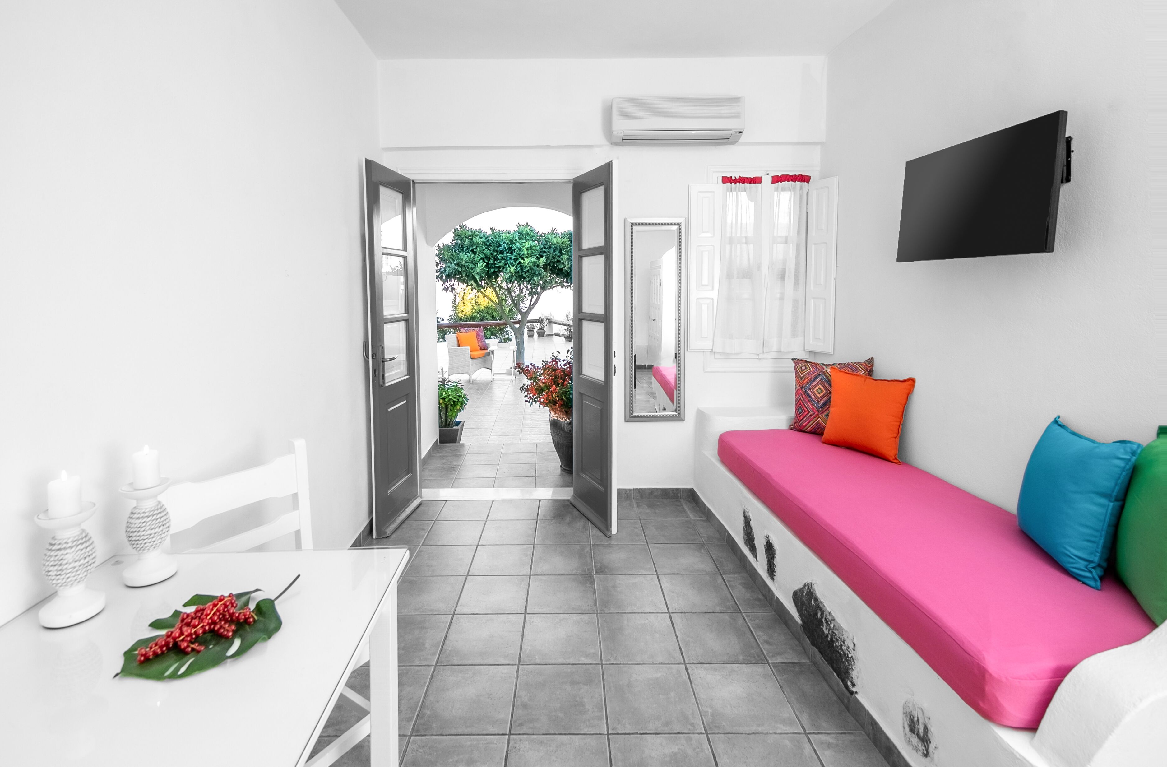 Une chambre moderne avec un canapé blanc, un téléviseur à écran plat et une vue sur un jardin, accessible par une porte ouverte.