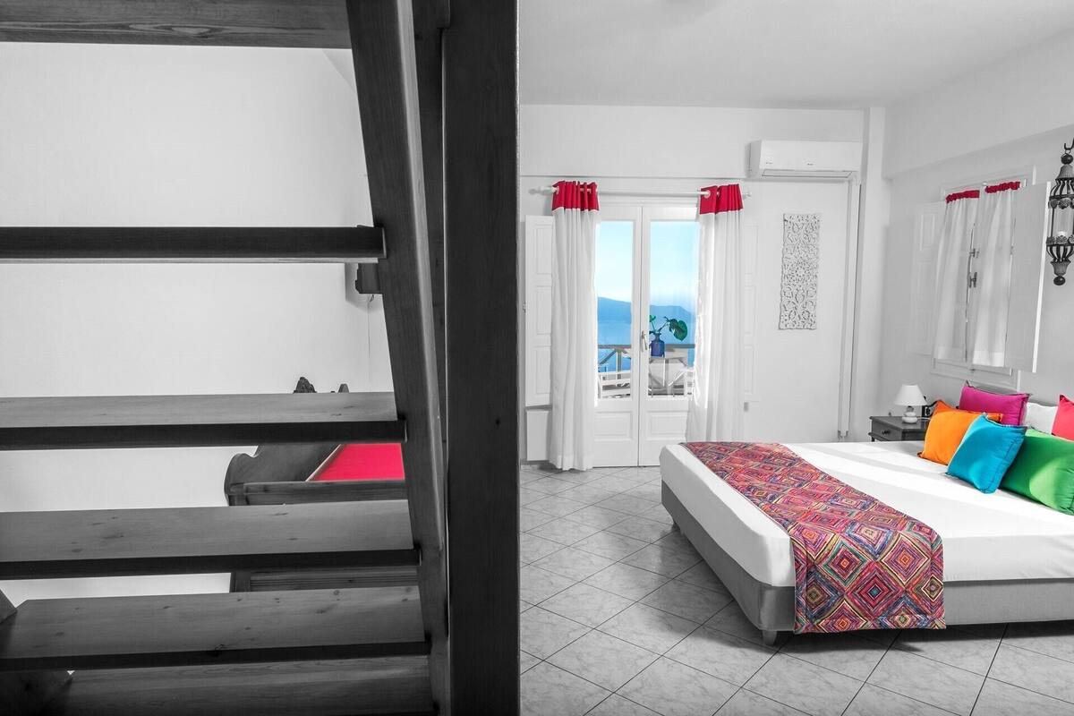 A bedroom with a bed, a nightstand, a window with curtains, and a view of the outdoors.