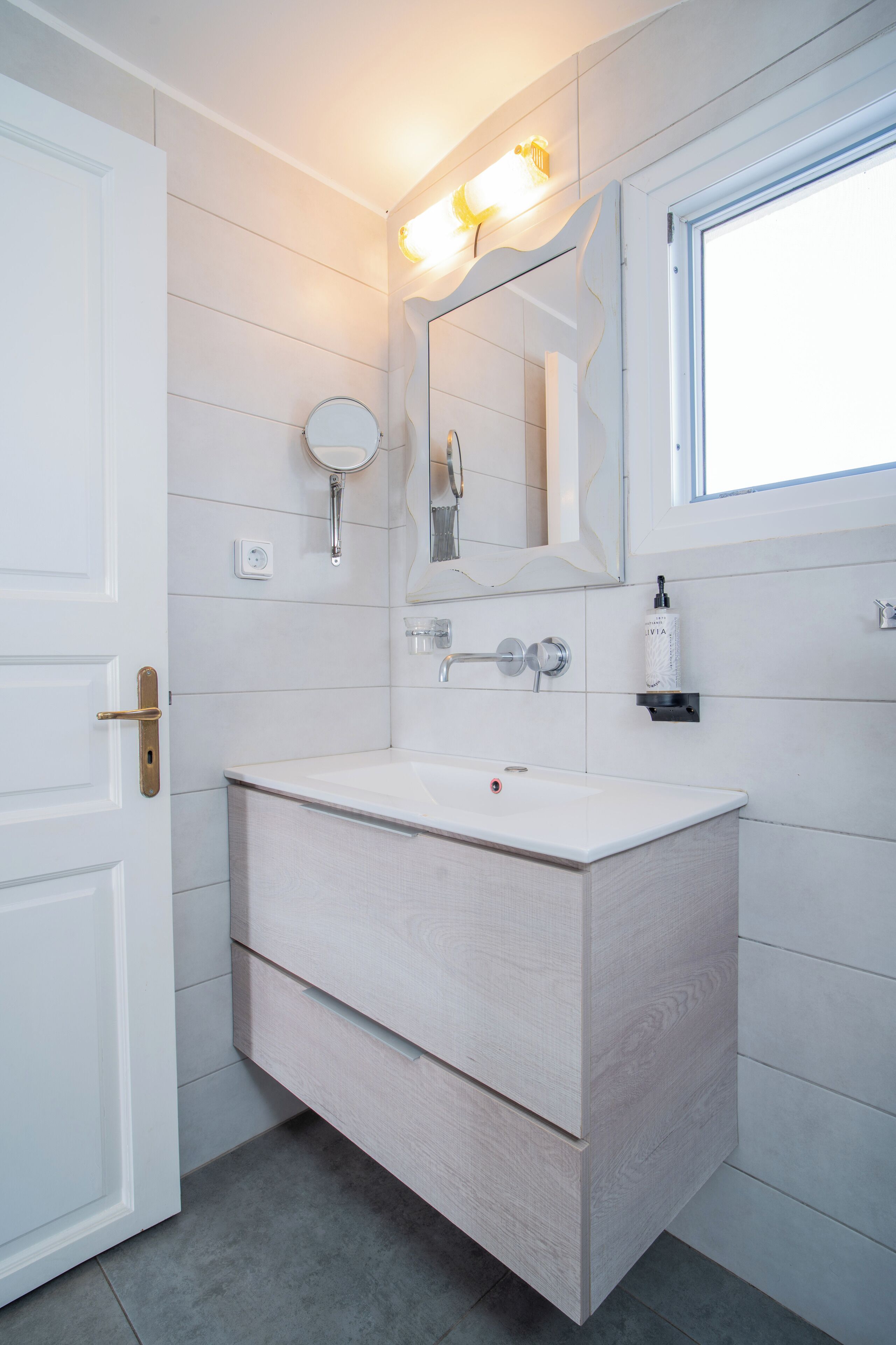A bathroom with a white vanity, a mirror, and a light fixture above the mirror.