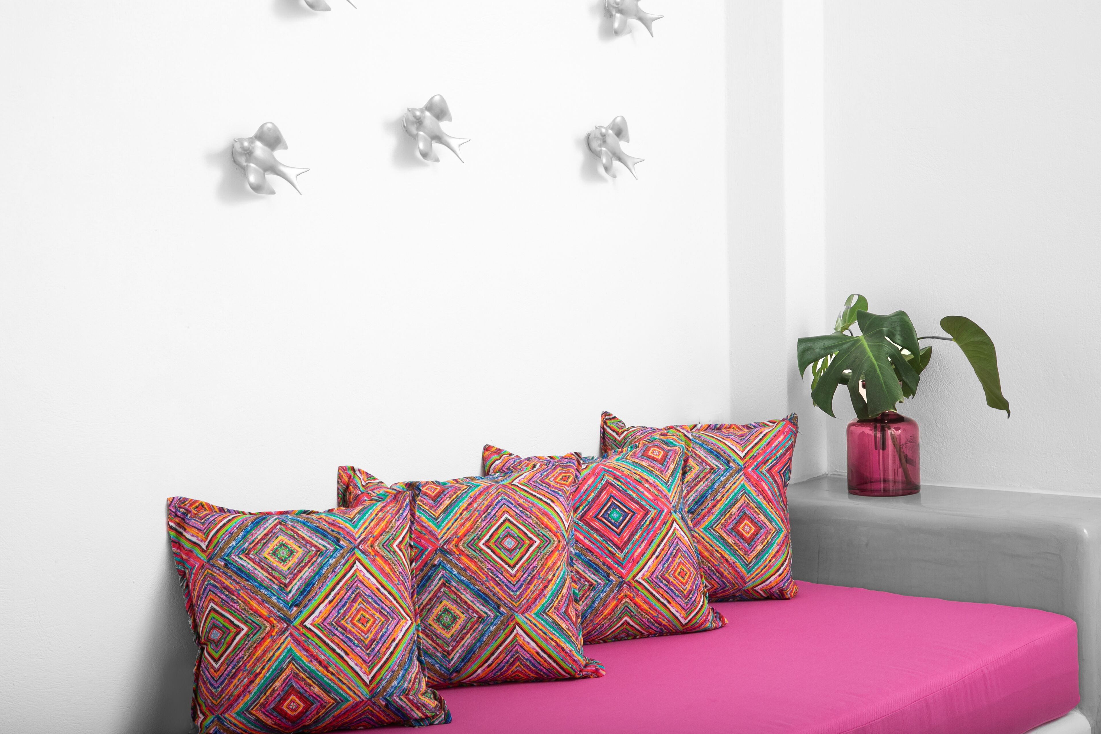 Ein Zimmer mit einem rosa Sofa, bunten Kissen mit Mustern, einer Topfpflanze und Wanddekorationen.