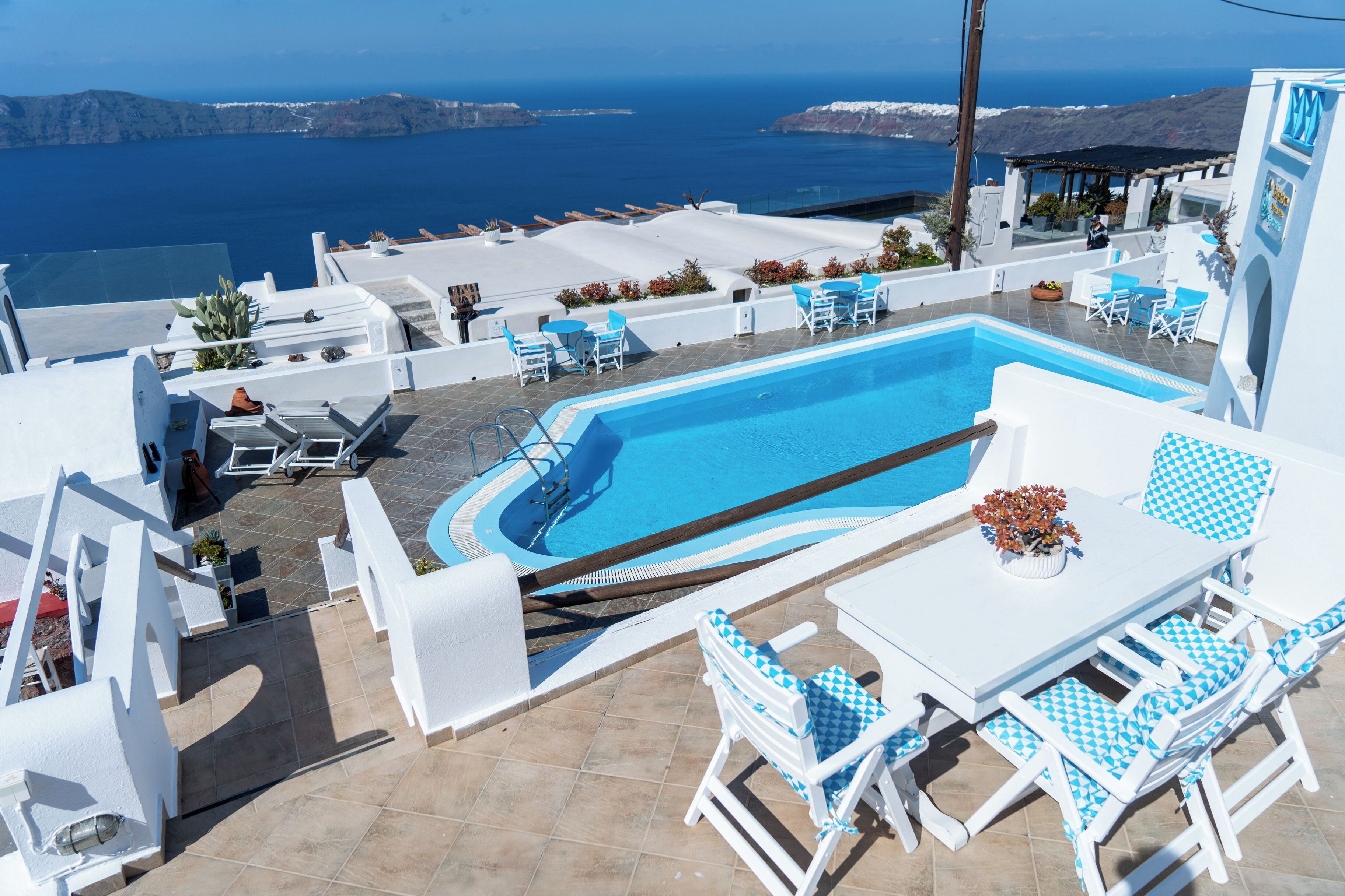 A rooftop pool with a view of the sea, white furniture, and a table with a vase of flowers.