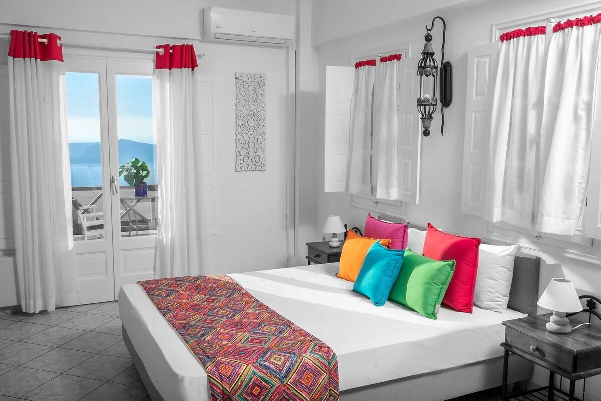 A bedroom with a bed, colorful pillows, a nightstand, a lamp, and a view through a door.