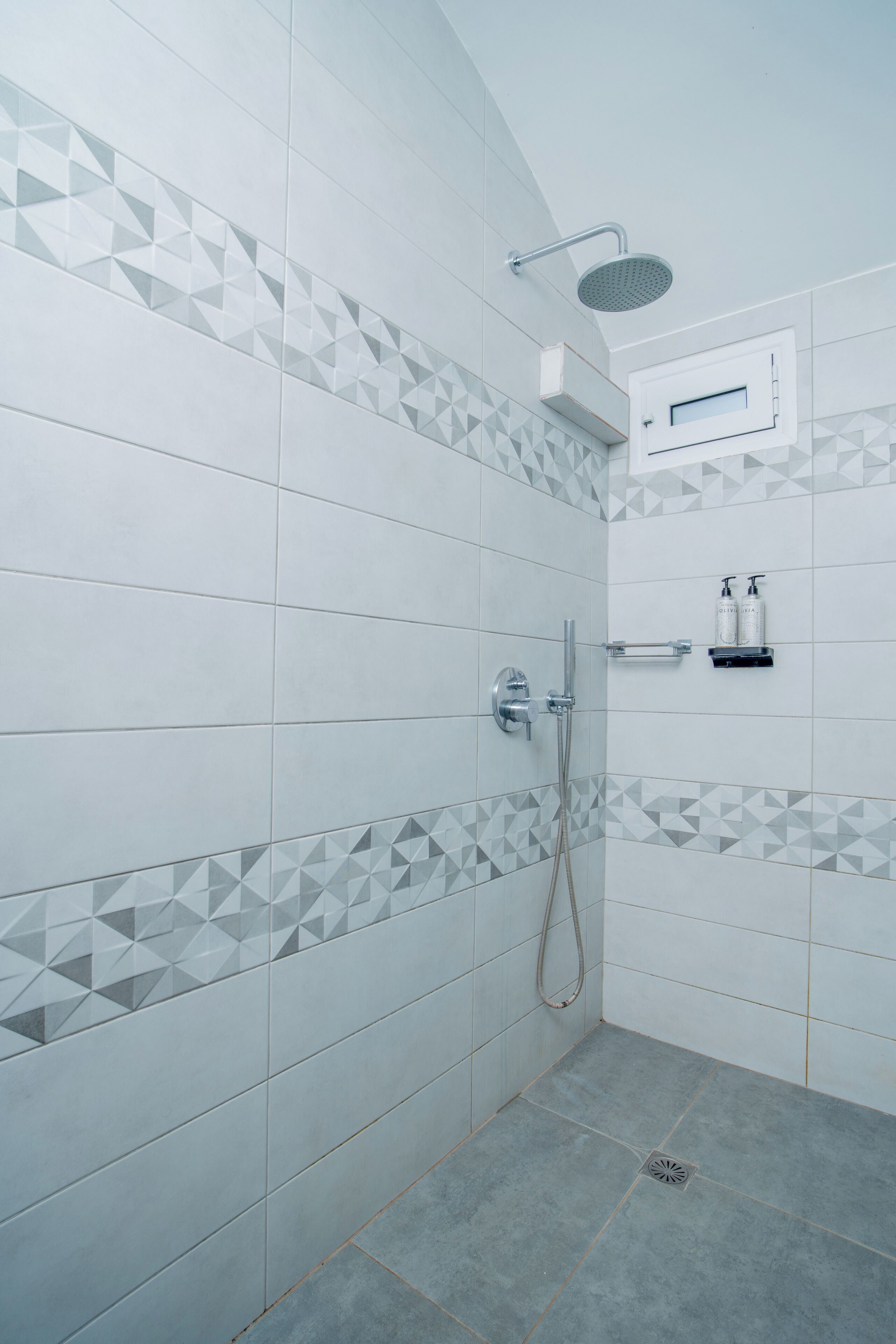 A modern bathroom with a shower, tiled walls, and a small shelf with toiletries.
