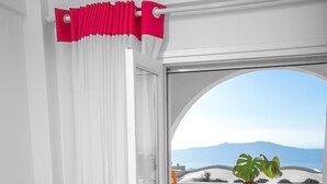 A modern room with a grey armchair, two round tables with plants, and a view of mountains through a large window. - Salvatore Caldera Suites (Santorini)
