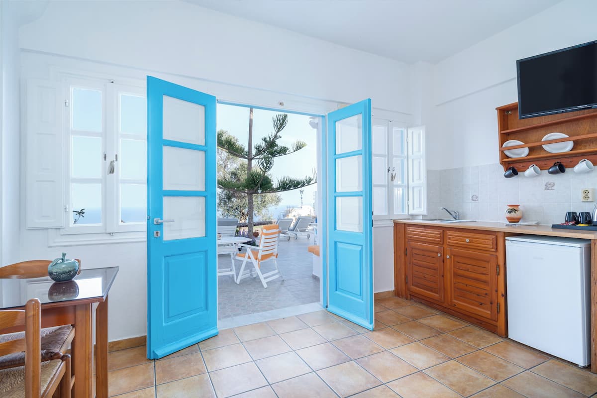 A kitchen with open blue doors leading to a patio area, a wooden cabinet, and a television mounted above the counter.