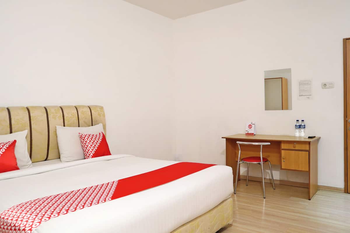 A hotel room with a bed, a desk, a chair, a mirror, and a door.