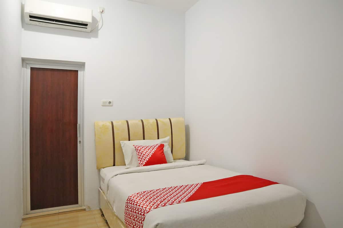 A small, clean room with a bed, a wooden door, and an air conditioning unit on the wall.