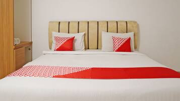 Cama com cabeceira bege, roupa de cama branca e detalhes vermelhos.