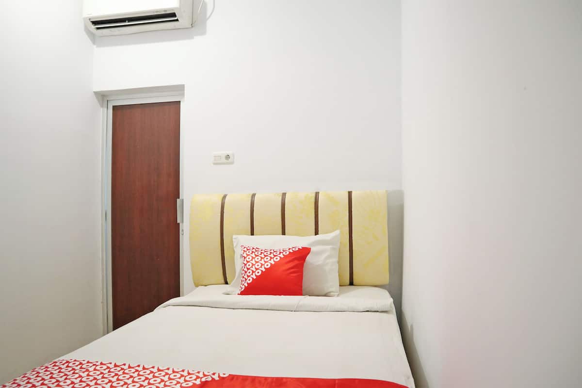 A single bed with a striped headboard, a red and white patterned pillow, and a white bedspread.