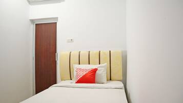 A single bed with a striped headboard, a red and white patterned pillow, and a white bedspread.