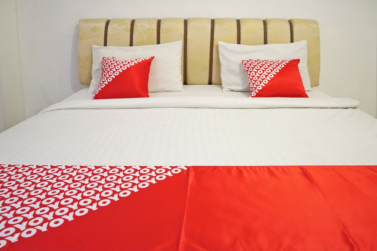 A bed with a white and red bedspread, two pillows with red and white patterns, and a headboard with vertical stripes.