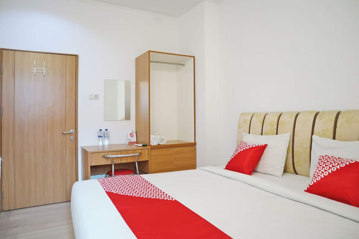 A hotel room with a bed, a desk, a chair, a wardrobe, and a mirror.