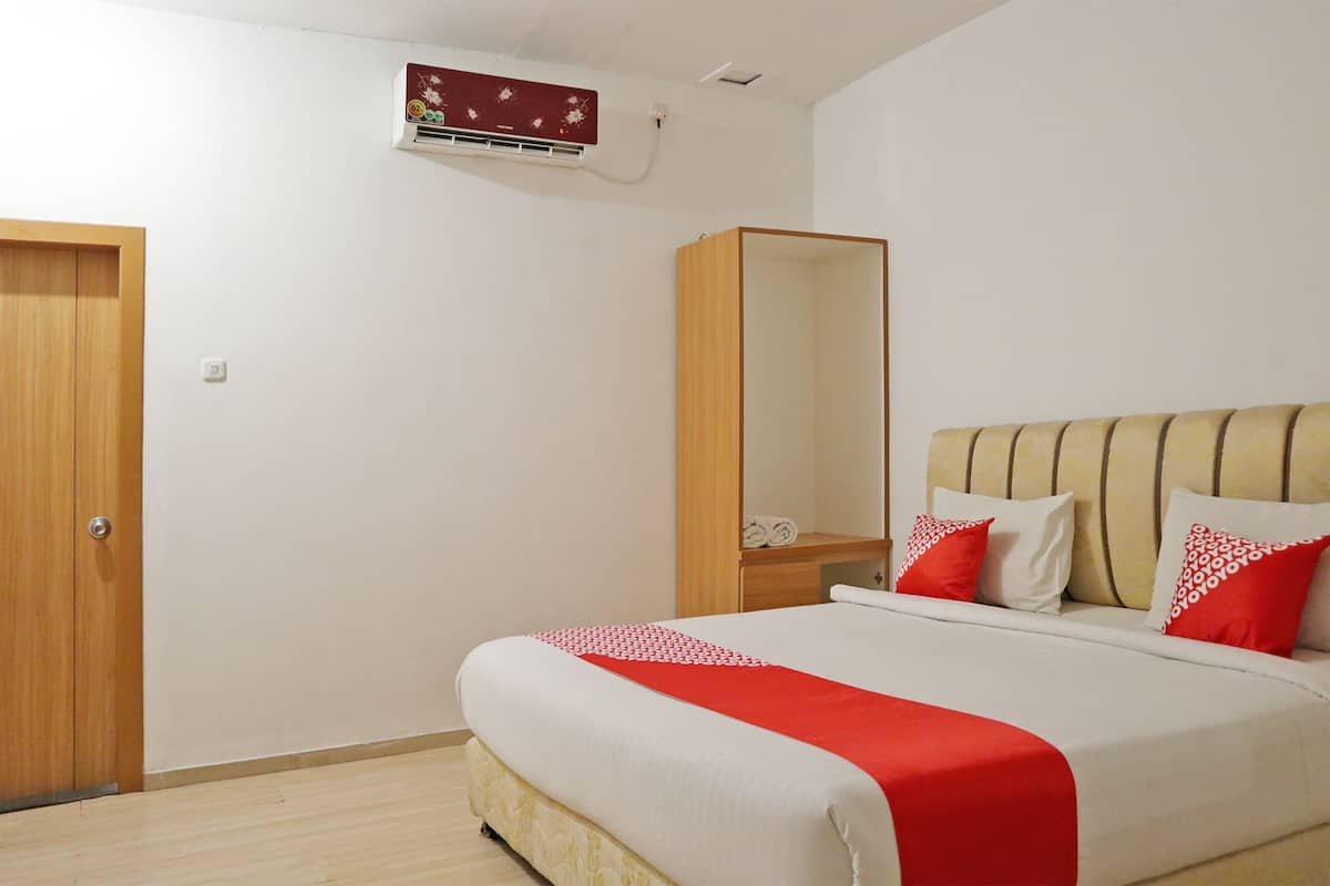 A bedroom with a bed, a wooden wardrobe, a mirror, and a wall-mounted air conditioner.