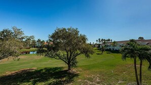 Un parcours de golf avec un grand arbre, un étang et un bâtiment doté d’un toit rouge en arrière-plan.