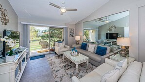 Un salon moderne avec un ventilateur de plafond, un ensemble de canapés, une table basse et un téléviseur.