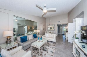 A spacious living room with a ceiling fan, a dining area with a chandelier, and a kitchen visible in the background.
