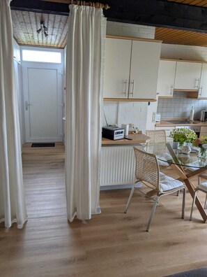 Une cuisine moderne avec des meubles blancs, une table à manger avec des chaises et une fenêtre avec des rideaux.