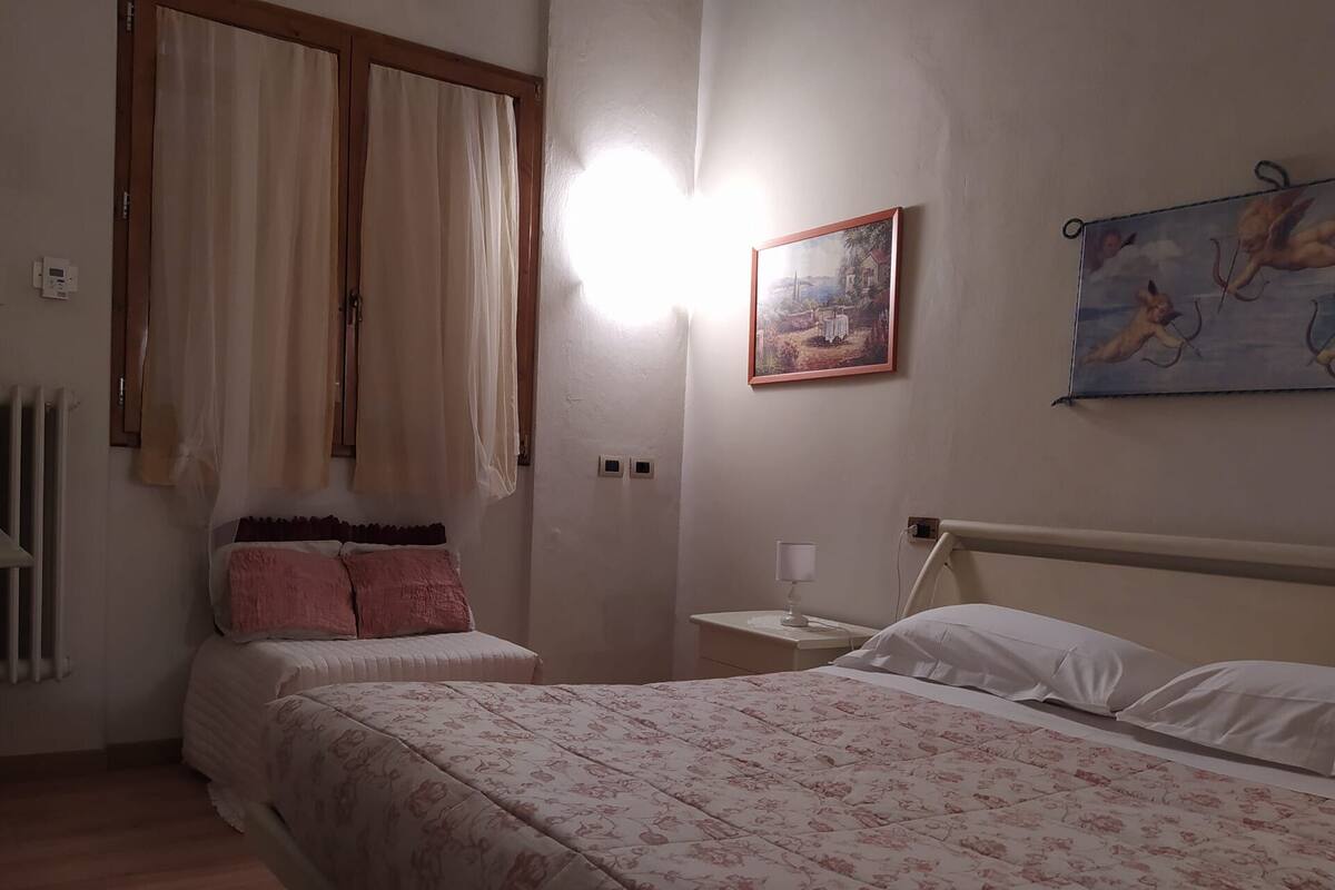 Een slaapkamer met twee bedden, een nachtkastje, een schilderij en een raam met gordijnen.